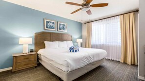 Una habitación de hotel con una cama, dos mesitas de noche, un ventilador de techo y una ventana con cortinas.