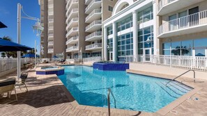 Un espace piscine d’hôtel avec une piscine à l’eau d’un bleu limpide, des chaises longues et un bâtiment doté de nombreux balcons.