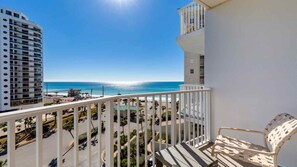 Un balcon offrant une vue sur l’océan et le paysage urbain, avec une chaise et une balustrade.