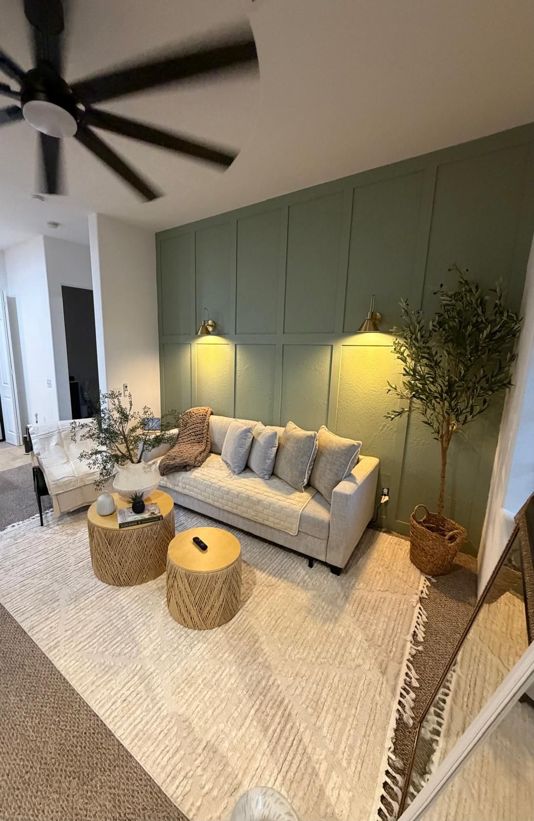 A modern living room with a sofa, two round side tables, a ceiling fan, and a wall-mounted light fixture.