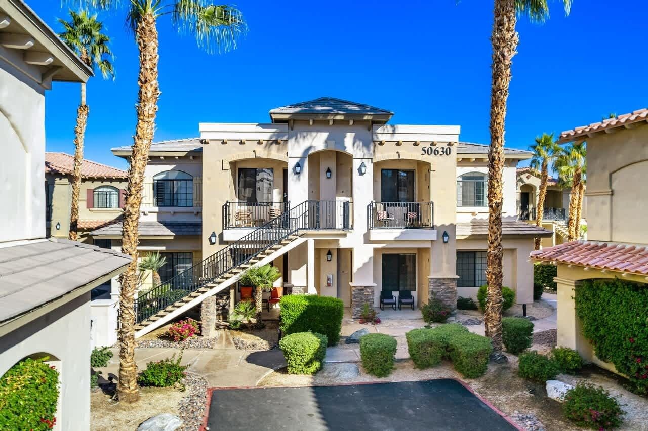 A multi-story building with a central courtyard, palm trees, and a clear blue sky.