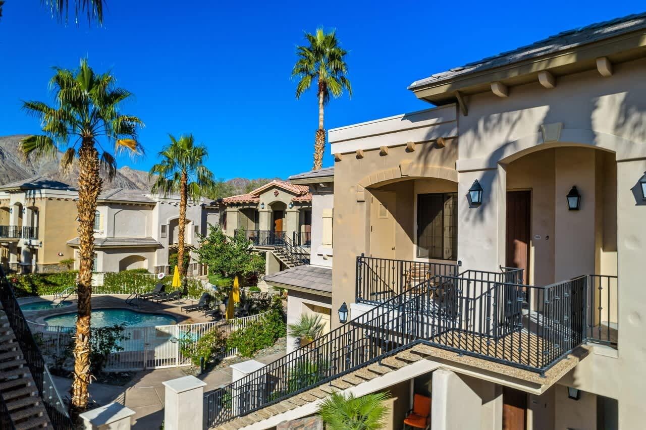 A residential area with a swimming pool, palm trees, and a balcony with a railing.