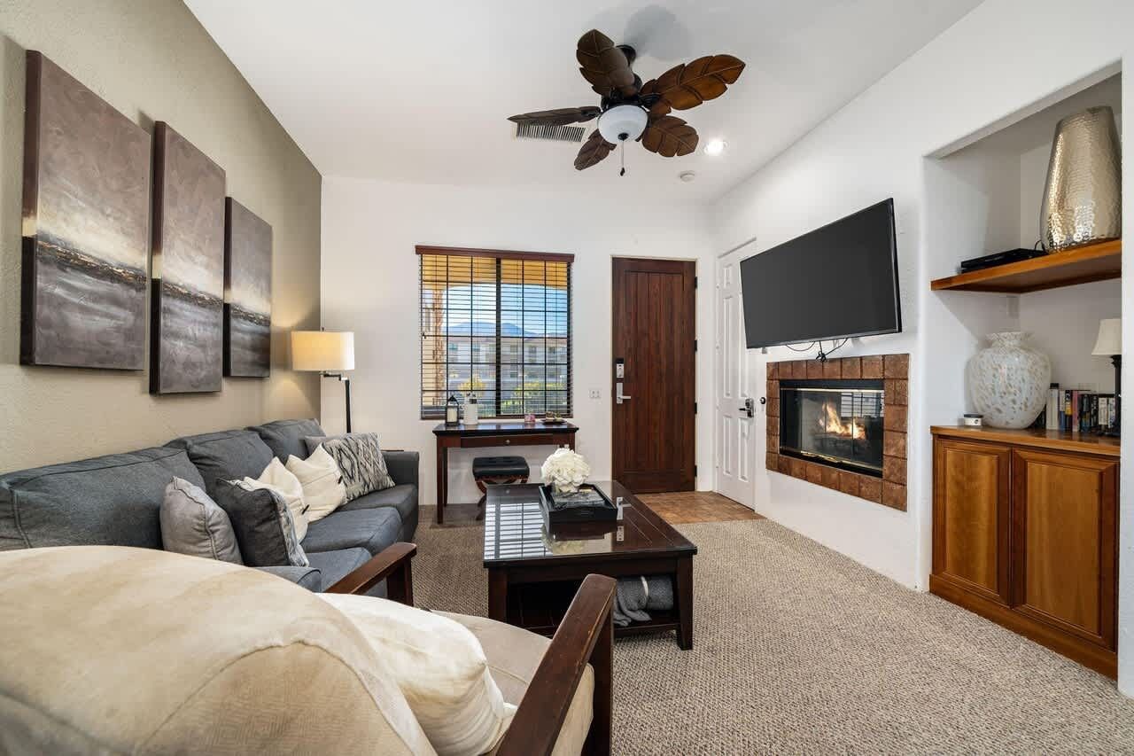 A living room with a sofa, coffee table, fireplace, television, and artwork on the wall.