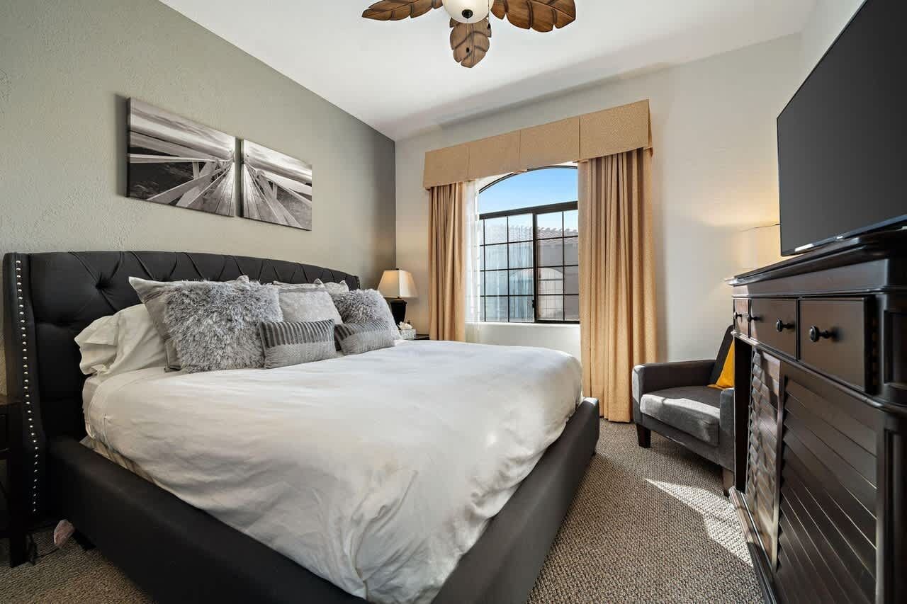 A hotel room with a large bed, a flat-screen TV, a sofa, and a window with curtains.