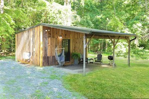 Una cabana de fusta rústica amb un porxo, una cadira penjant i una zona de barbacoa.