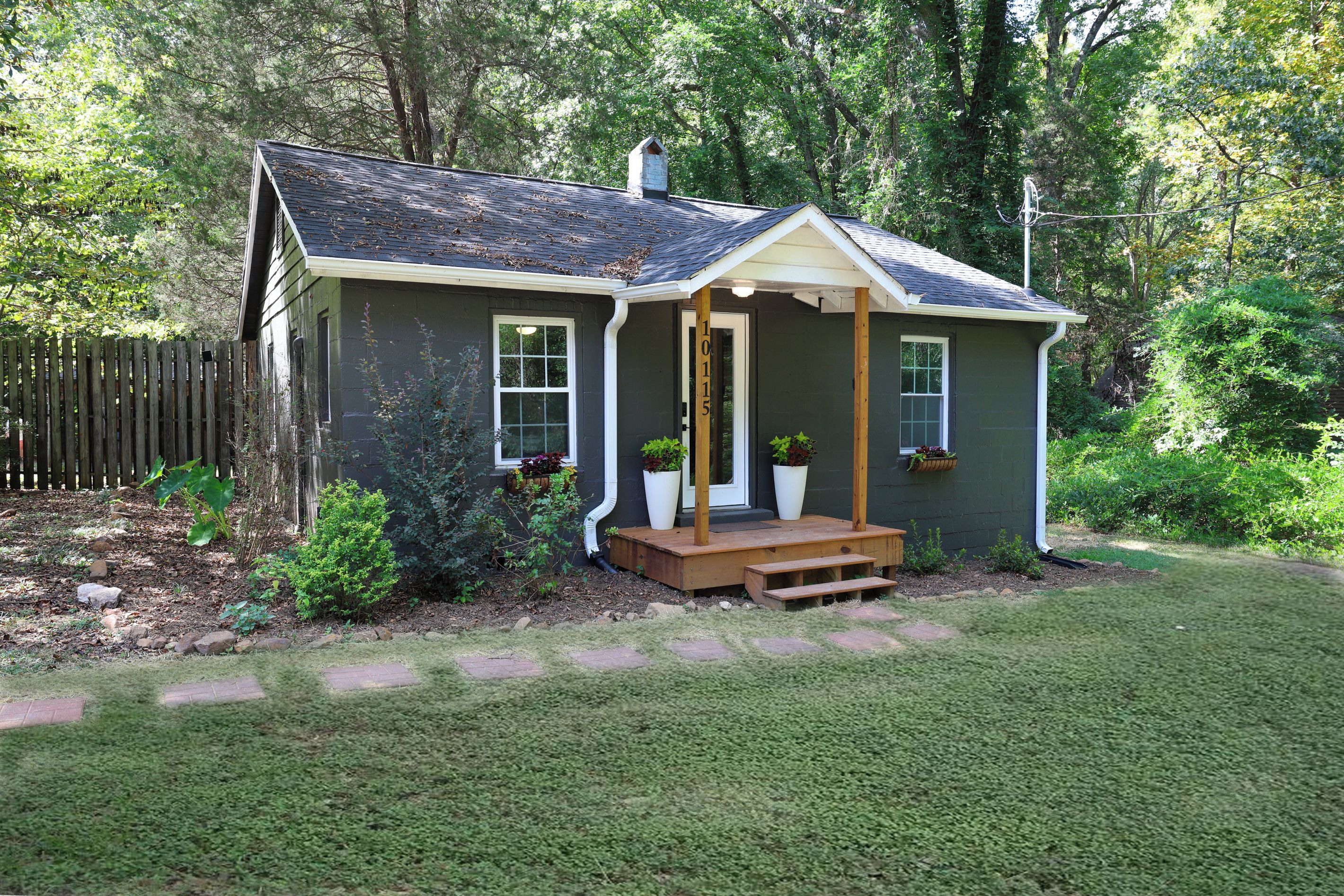 A small house with a porch, a number '10115' on the door, and a fenced yard.