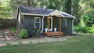 A small house with a porch, a number '10115' on the door, and a fenced yard.