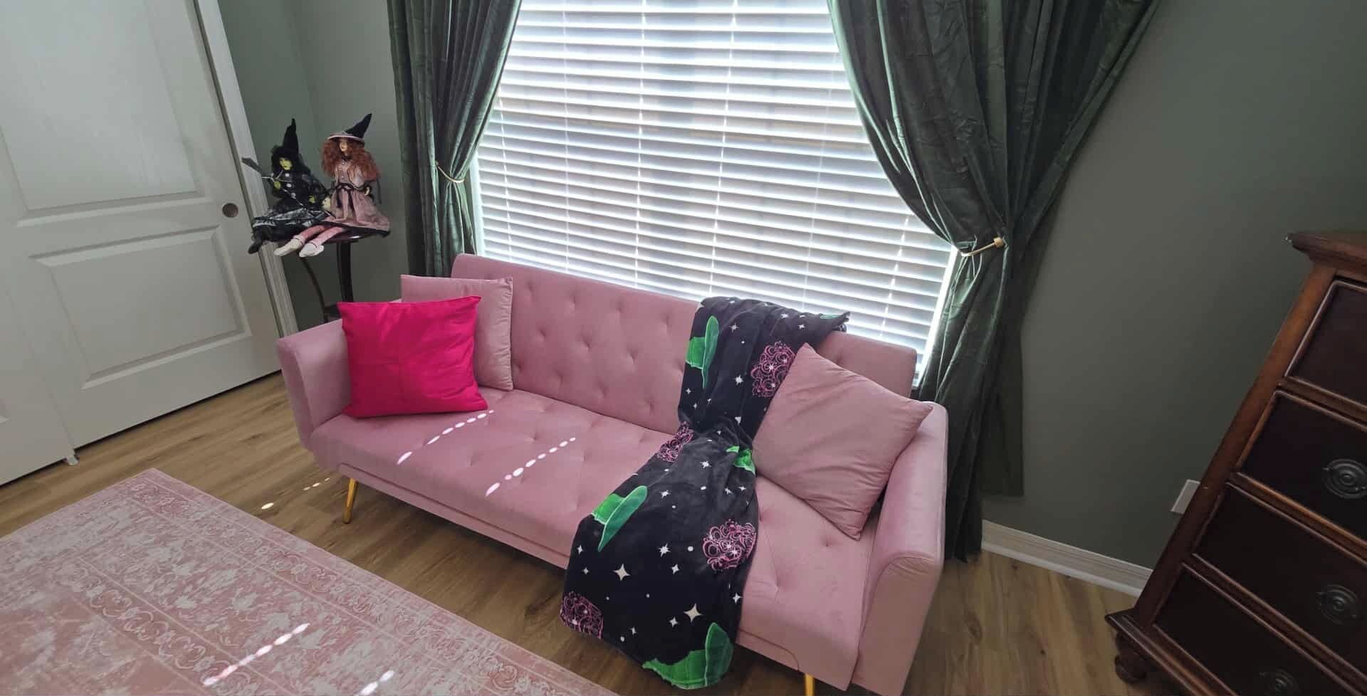 A room with a pink sofa, a wooden cabinet, a patterned rug, and a window with curtains.