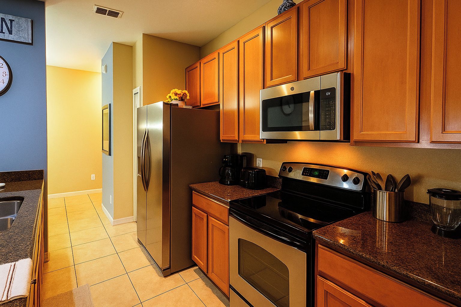 A kitchen with wooden cabinets, a stainless steel refrigerator, a microwave, an oven, and a coffee maker.