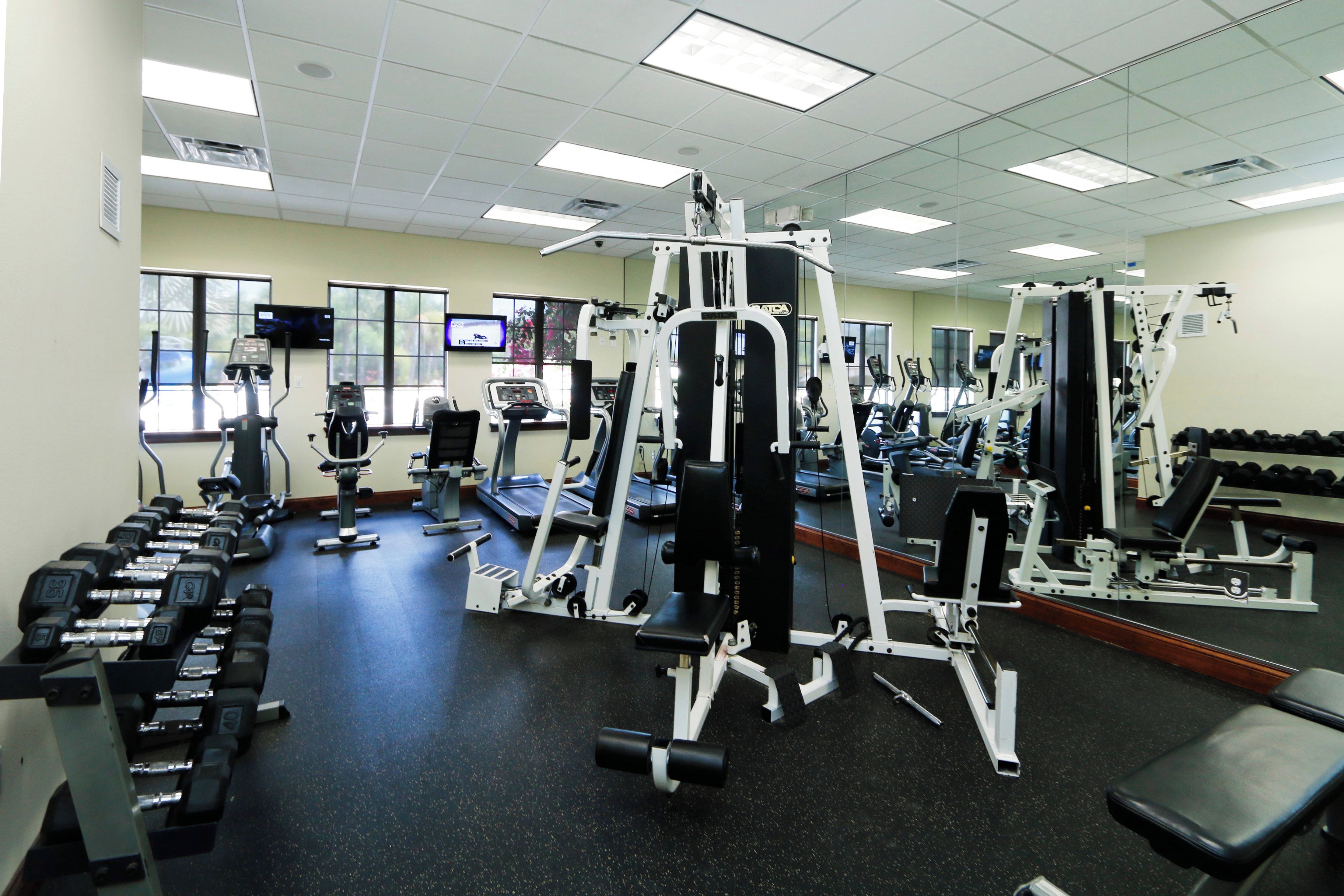 A gym with various exercise equipment, treadmills, and dumbbells.