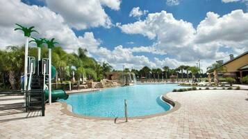 A swimming pool with a water slide, palm trees, and a clear sky.