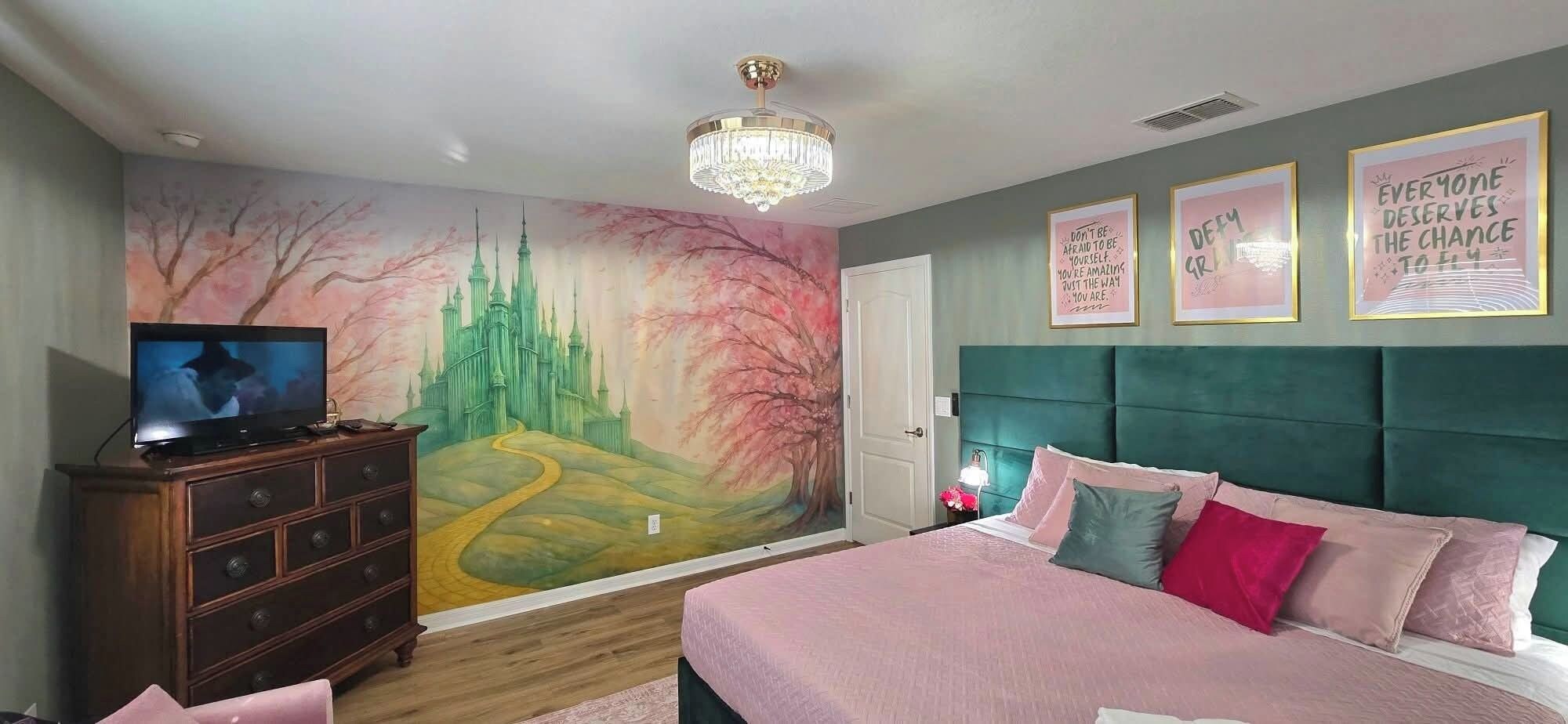 Een slaapkamer met een groot bed, een dressoir, een televisie, een muurschildering en motiverende wanddecoratie.