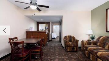 A hotel room with a dining area, a sofa, a chair, a lamp, and a ceiling fan.