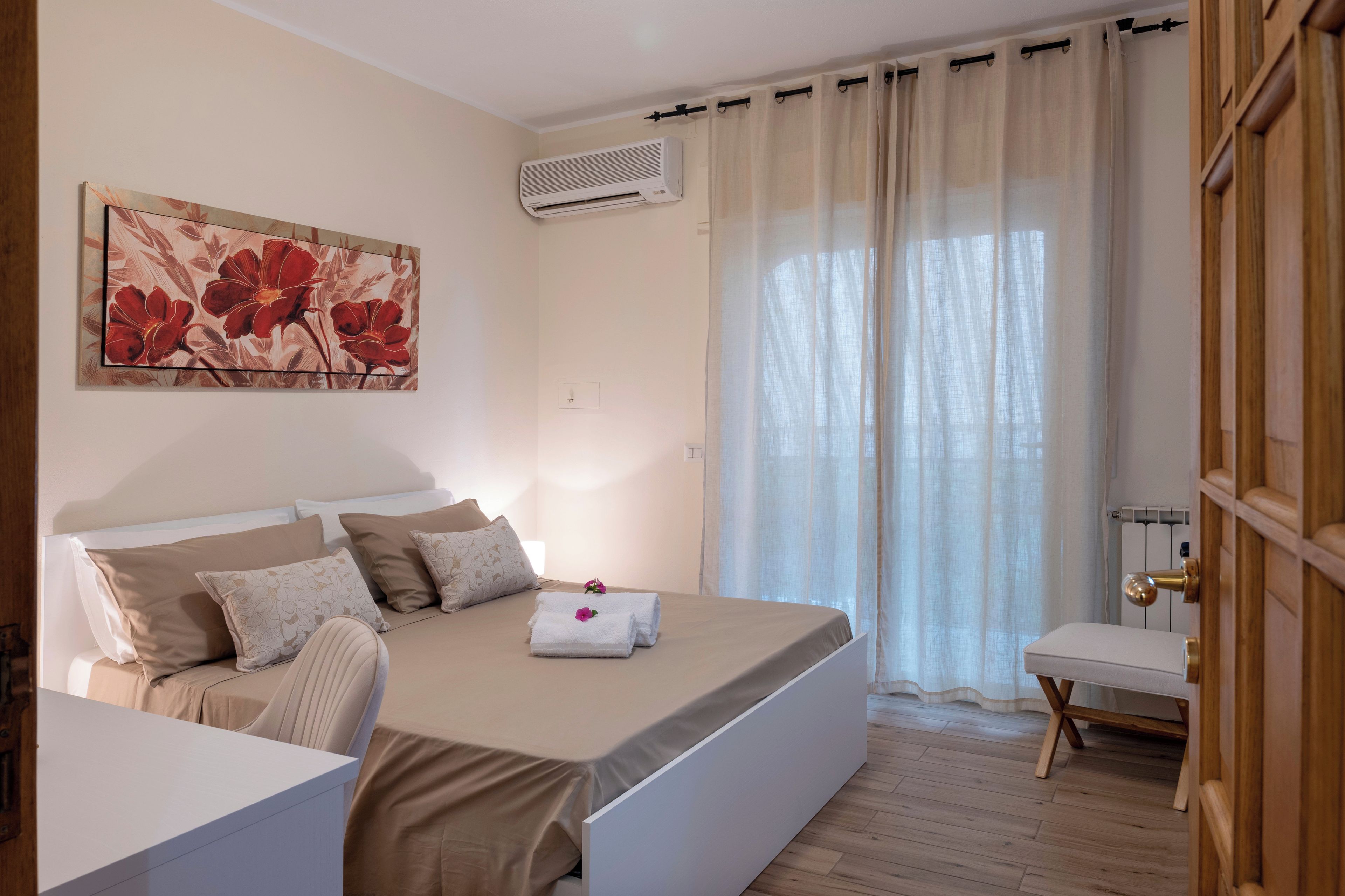 Una camera d'albergo con un letto, una scrivania, una sedia, un quadro, un condizionatore d'aria e una finestra con tende.