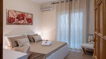 Una camera d'albergo con un letto, una scrivania, una sedia, un quadro, un condizionatore d'aria e una finestra con tende.