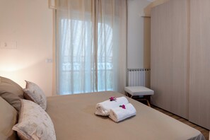 A hotel room with a bed, a small bedside table, a radiator, and a window with sheer curtains. - Don Alfio Vacation Home (Taormina)