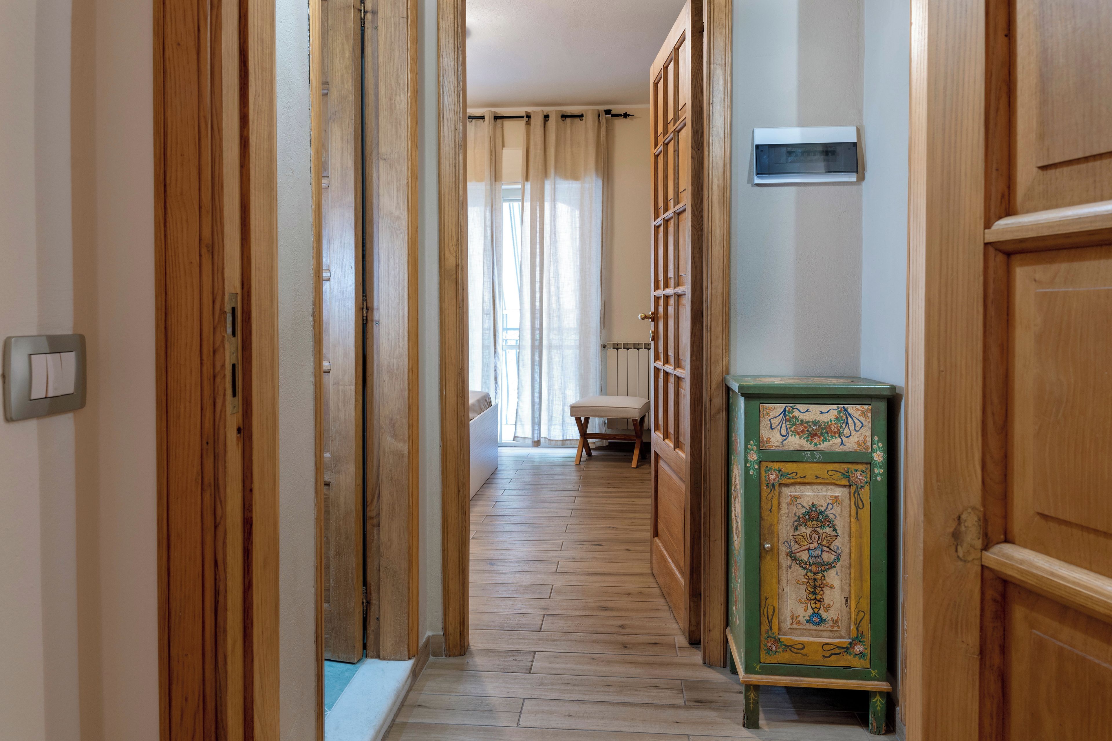 Un corridoio con porte in legno, un termosifone, una panca e un armadietto decorato con motivi floreali.