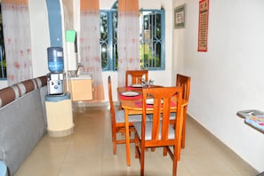 Un comedor con una mesa, sillas, dispensador de agua y una ventana con cortinas.