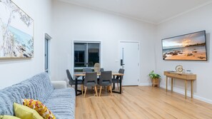 Un salon moderne avec un canapé, une table à manger, des chaises, un téléviseur et des œuvres d’art accrochées aux murs.