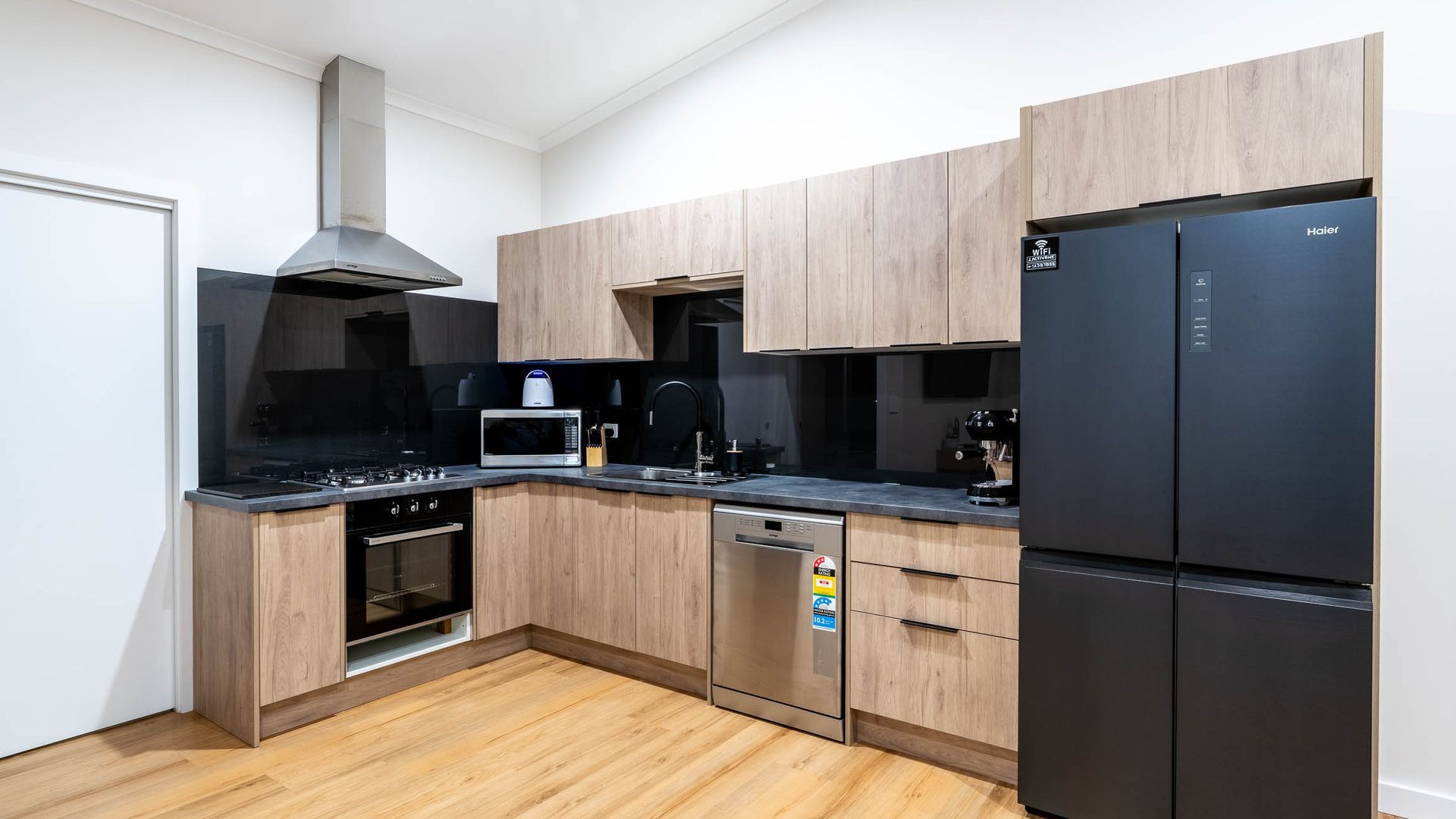 Une cuisine moderne avec des meubles en bois, un réfrigérateur noir, un four à micro-ondes, une cuisinière et un lave-vaisselle.