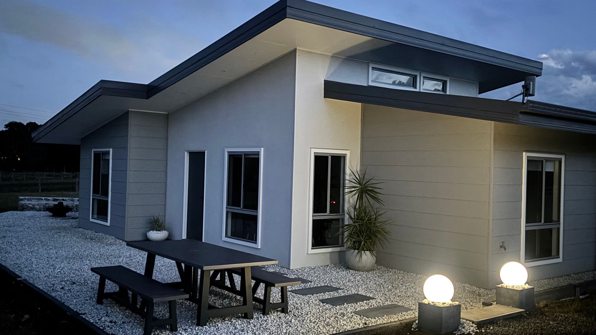 Une maison moderne à deux étages, dotée d’un patio, d’un espace salon extérieur et d’une entrée bien éclairée.