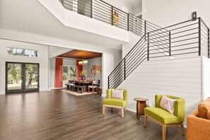 A spacious living area with a staircase, wooden flooring, and modern furniture. - Boots & Birdies -Sleeps 22- Luxury Pool+Spa, Pickleball, Golf Simulator, & more (Austin)