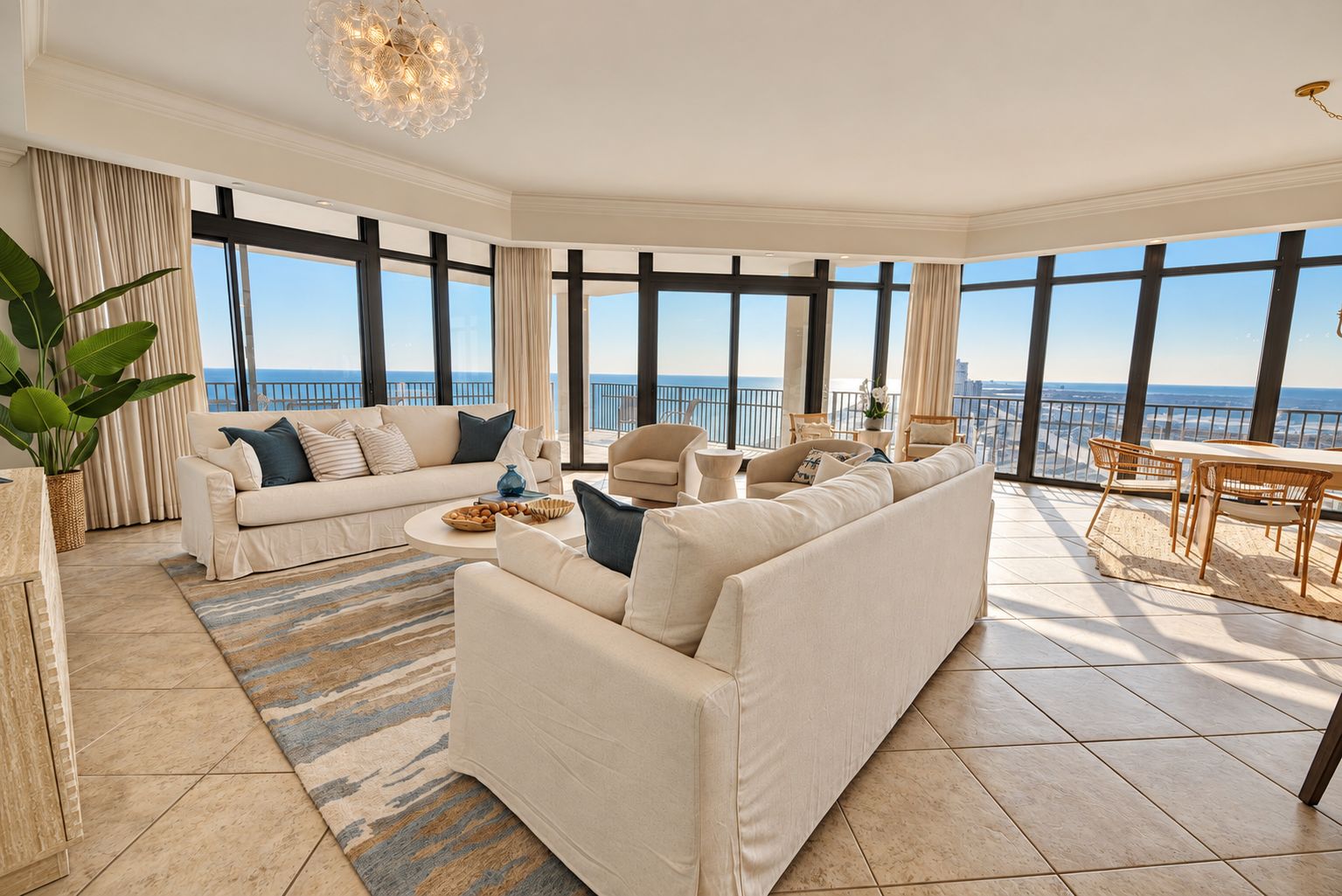 A spacious living room with a large window, a sofa set, a coffee table, and a dining area with chairs.