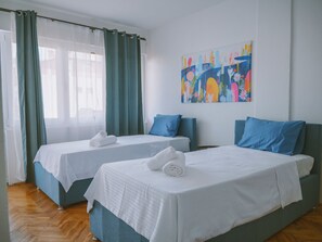 A hotel room with two beds, a large window with curtains, and a colorful abstract painting on the wall.