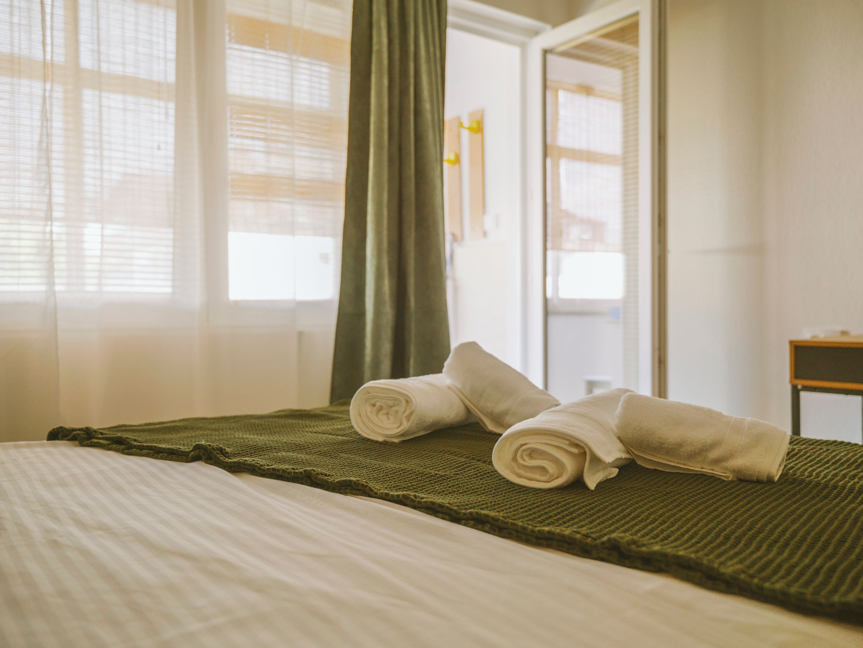 A hotel room with a bed, a green blanket, and two rolled towels.