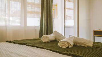 A hotel room with a bed, a green blanket, and two rolled towels.