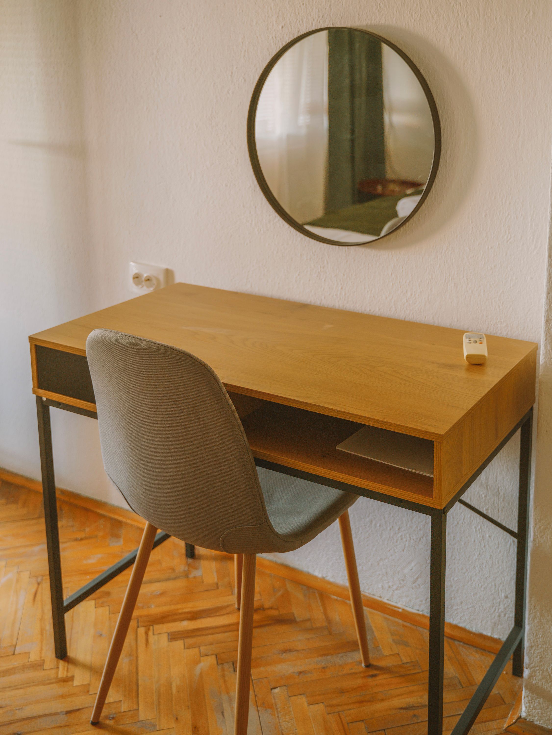 Un escritorio de madera con una silla, un espejo redondo en la pared y un enchufe.