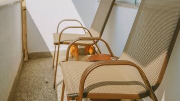 A balcony with two metal chairs and a table, a window, and a white wall.