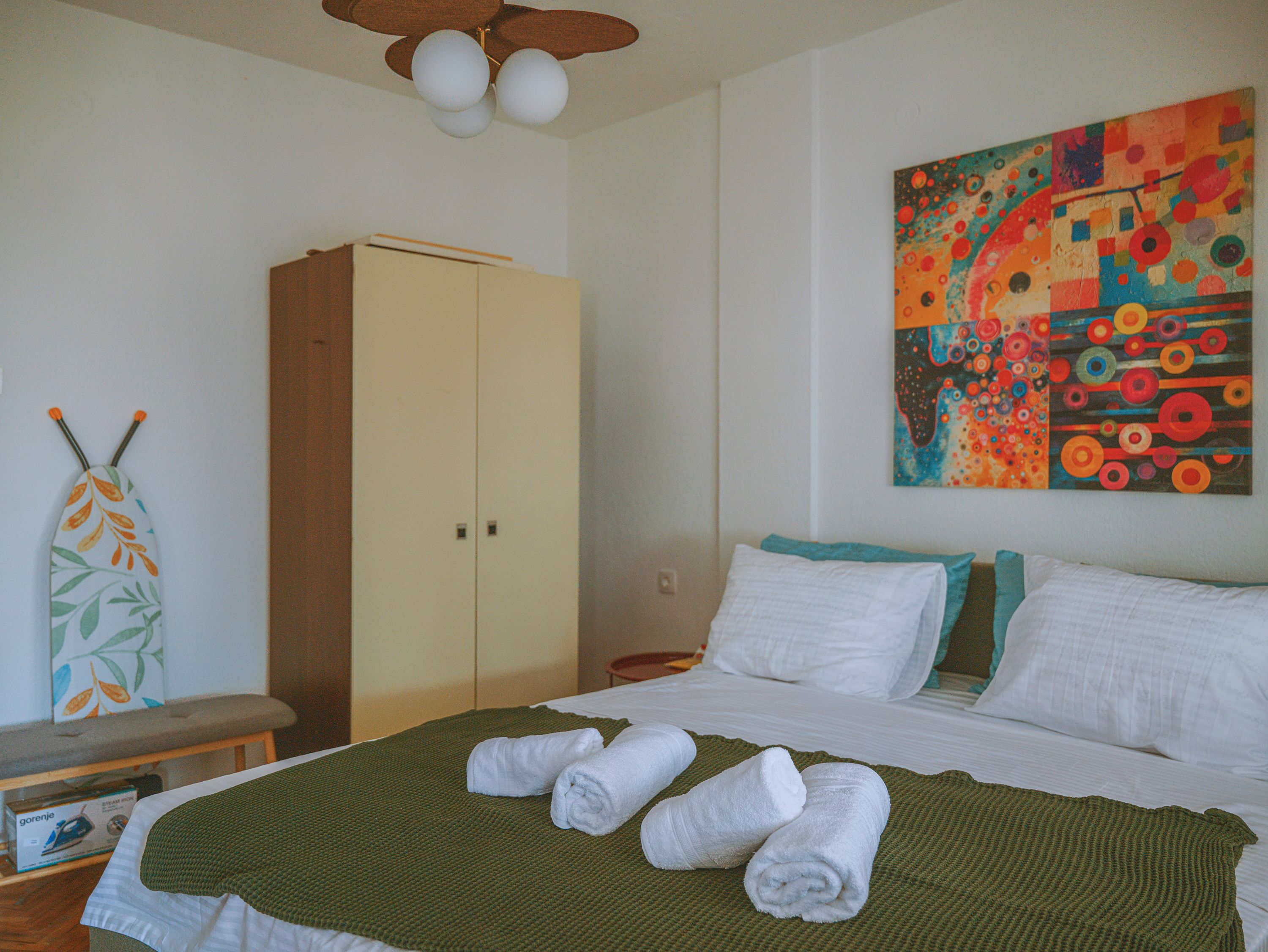 A bedroom with a bed, a wardrobe, a painting, and a towel rack.