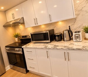 Una cocina moderna con armarios blancos, una estufa negra, un microondas, una tetera y un tostador.