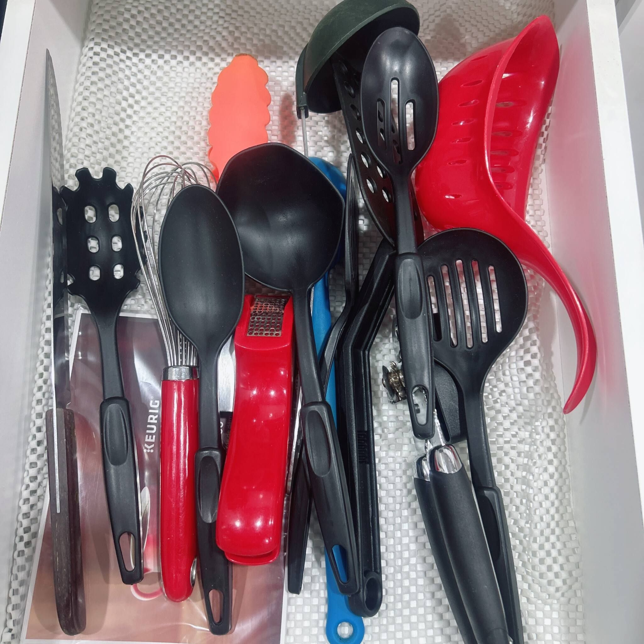 A drawer containing various kitchen utensils including a red spatula, a black spatula, and a blue spatula.
