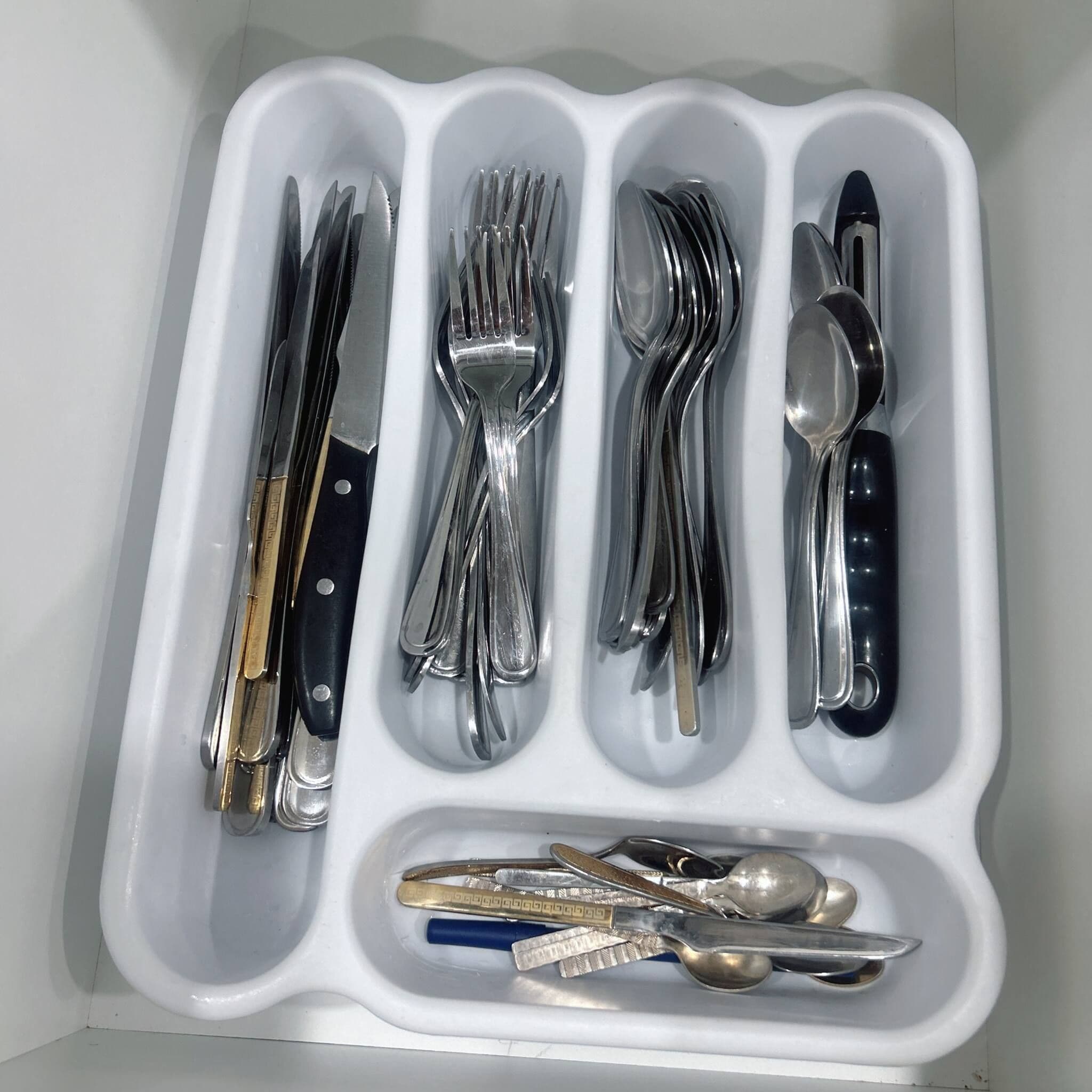 A white tray with various cutlery items including forks, knives, spoons, and a pair of scissors.