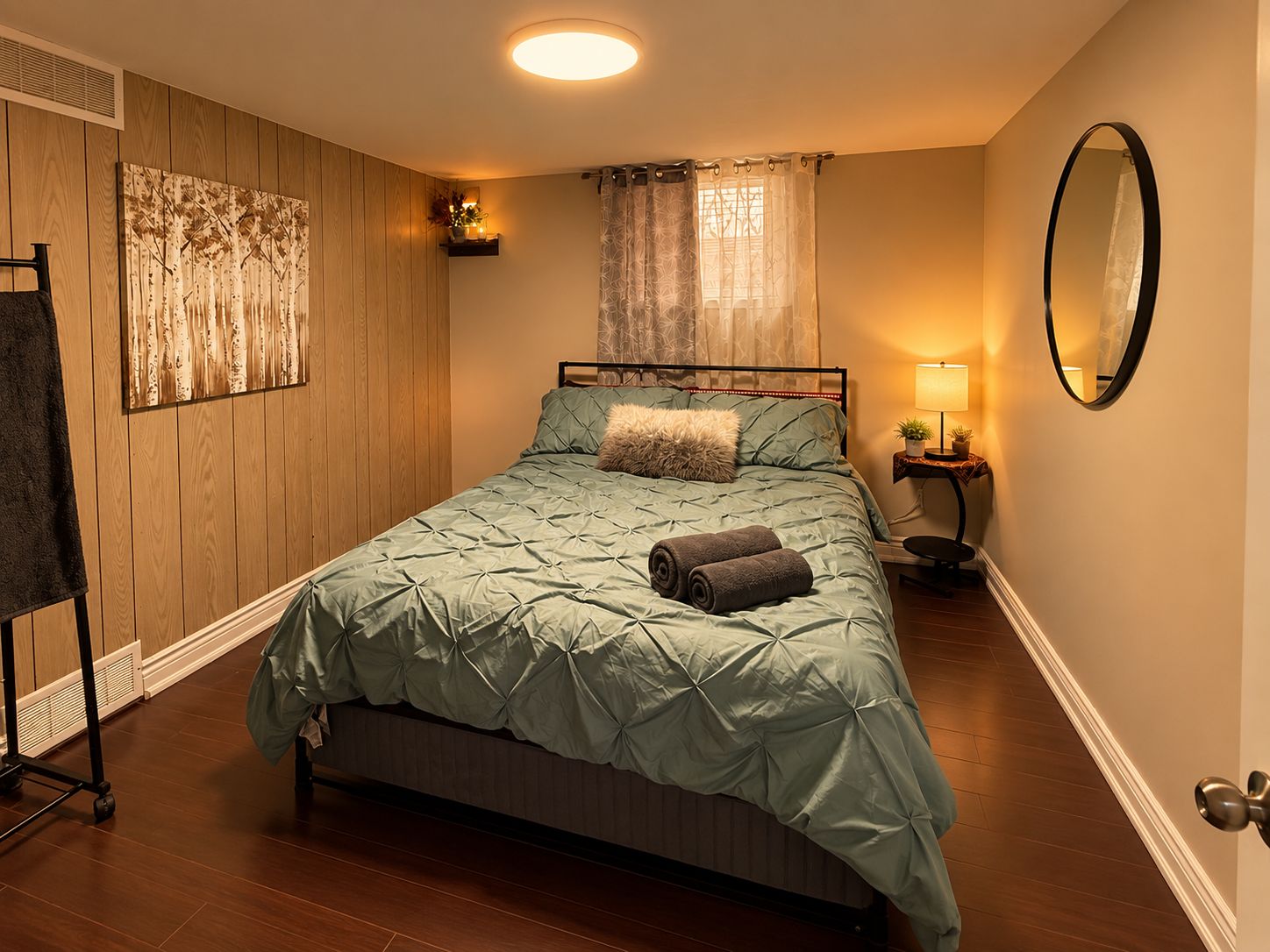 A bedroom with a bed, a nightstand, a mirror, a wall-mounted shelf, and a window with curtains.