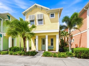 A two-story yellow house with a porch, surrounded by greenery and adjacent to other houses. - Key Lime Dream Cottage near Disney | Margaritaville & Waterpark Access - 3074KL (Kissimmee)