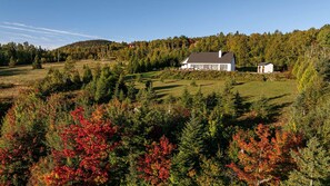 A house surrounded by a forested area with a clear sky. - L'Aquarelle : Riverfront Home, 180° View & Hot Tub (Saint-Irénée)