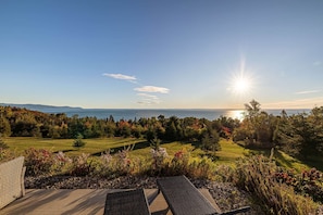 A patio with outdoor furniture overlooking a scenic landscape with a view of the sea and distant mountains. - L'Aquarelle : Riverfront Home, 180° View & Hot Tub (Saint-Irénée)