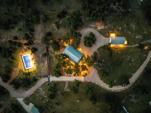 Une vue aérienne d’une propriété comprenant un court de tennis, un bâtiment avec un toit bleu et une route sinueuse.