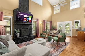 A living room with a fireplace, a flat-screen TV mounted above it, and a dining area with a table and chairs. - Private 10-Acre Estate · Heated Pool · Sleeps 24 (Fredricksburg)
