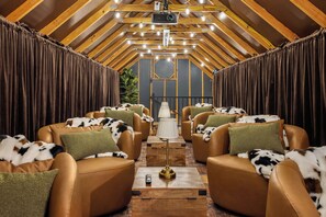 A cozy room with leather sofas, a central table, and a ceiling projector. - Private 10-Acre Estate · Heated Pool · Sleeps 24 (Fredricksburg)