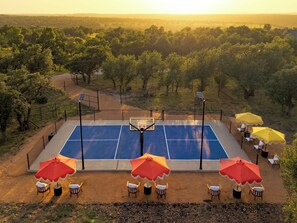 An outdoor basketball court with seating and umbrellas, surrounded by trees. - Romantic Hill Country Cottage w/ Private Hot Tub (Fredricksburg)