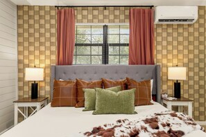 Un dormitorio con cabecera capitonada, cama con almohadas marrones y verdes, colcha blanca y manta mullida marrón y blanca.