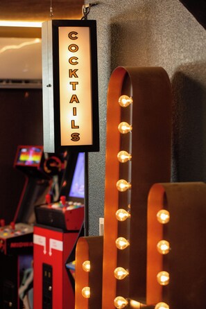 A sign for a cocktail bar area with illuminated letters, a red machine with buttons, and a wall with a textured surface. - 40-ft Heated Pool & Spa, Sport Court, Game Room (Fredricksburg)