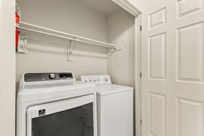 A laundry room with a front-loading washer and dryer, a drying rack, and a door with a handle. - 40-ft Heated Pool & Spa, Sport Court, Game Room (Fredricksburg)