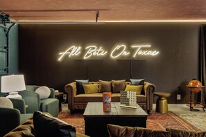 A modern living room with a neon sign reading 'All Bets On Texas,' a brown leather sofa, a green armchair, a coffee table, and a globe on a stand. - 40-ft Heated Pool & Spa, Sport Court, Game Room (Fredricksburg)