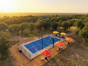 Ein Basketballplatz im Freien mit Netz, umgeben von Bäumen und mit Gartenmöbeln sowie Sonnenschirmen ausgestattet.