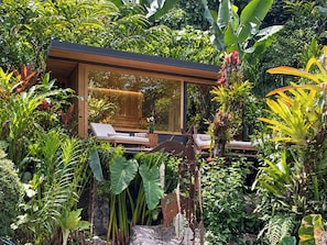 Un área de lounge moderna al aire libre con terraza de madera, asientos y exuberantes plantas tropicales.
